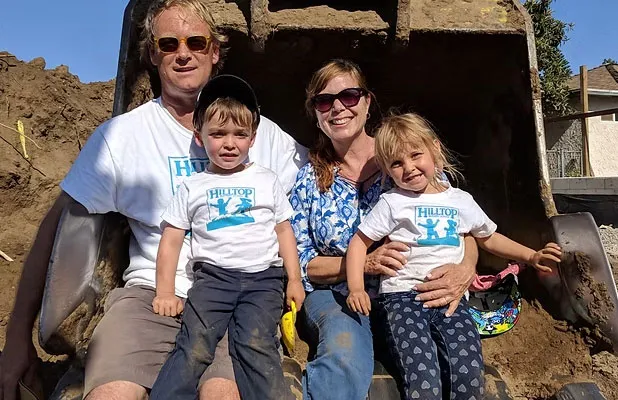 Family of four wearing sunglasses smiling in front of a large wooden barrel or container outdoors